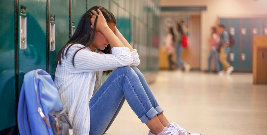 Image of a female high school student sitting on the floor by her locker, head in hands