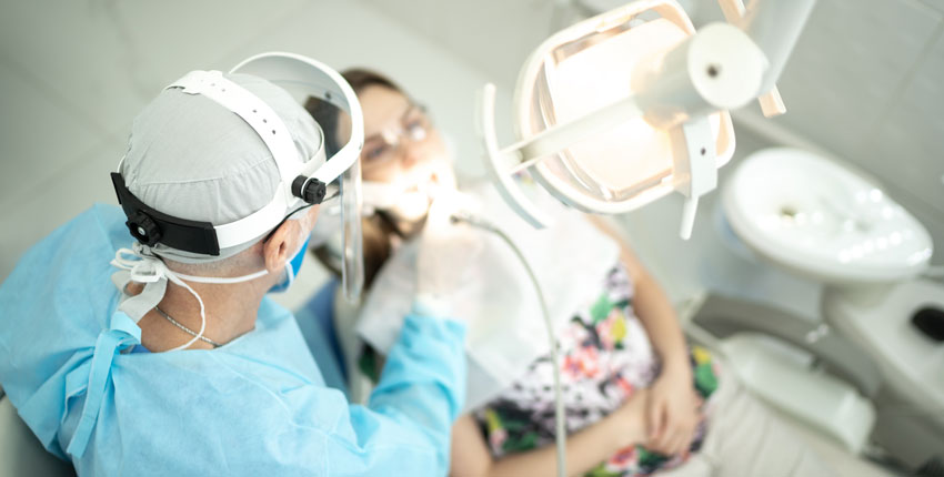 Dentist in PPE working on patient in a dentist's chair 