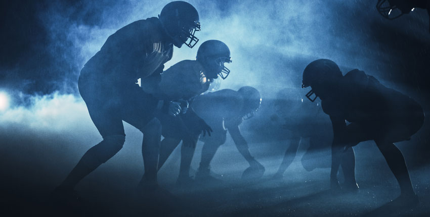 Backlight photo of football players in silhouette on playing field