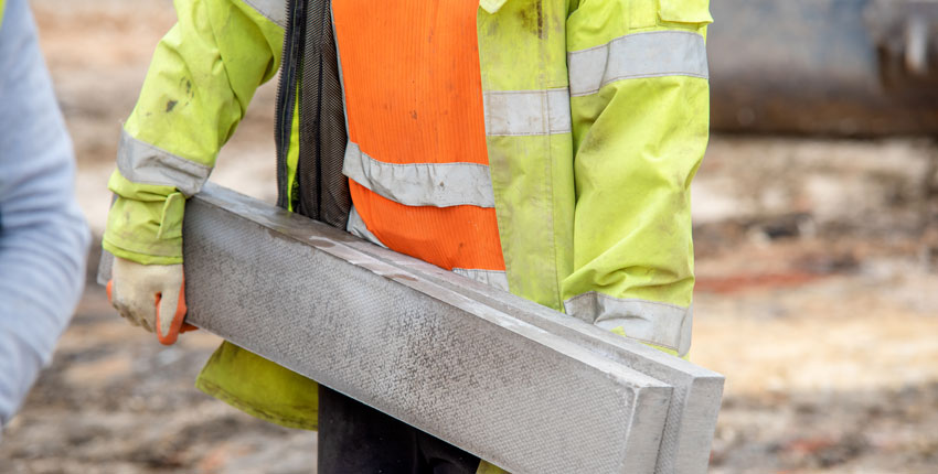 Photo of a construction worker carrying a large concrete beam 