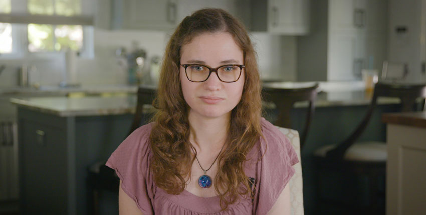 A shot of Jessica Chaikof from the chest up, wearing a pink shirt and glasses