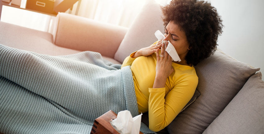 A sick person blowing their nose on a couch