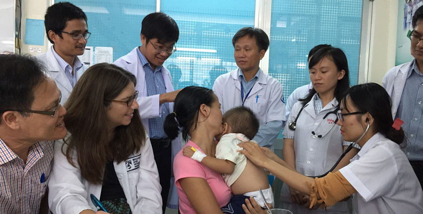 Photo of a group of medical students in Vietnam looking on as a baby is being examined in clinic. 