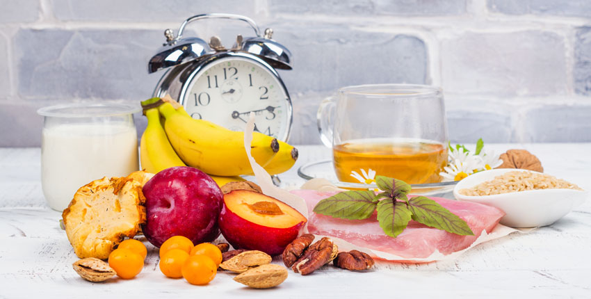 Photo of a bunch of fruit and food with an alarm clock nearby