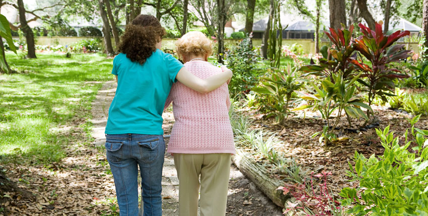 Caregiver walking with an elderly woman, photographed from behind