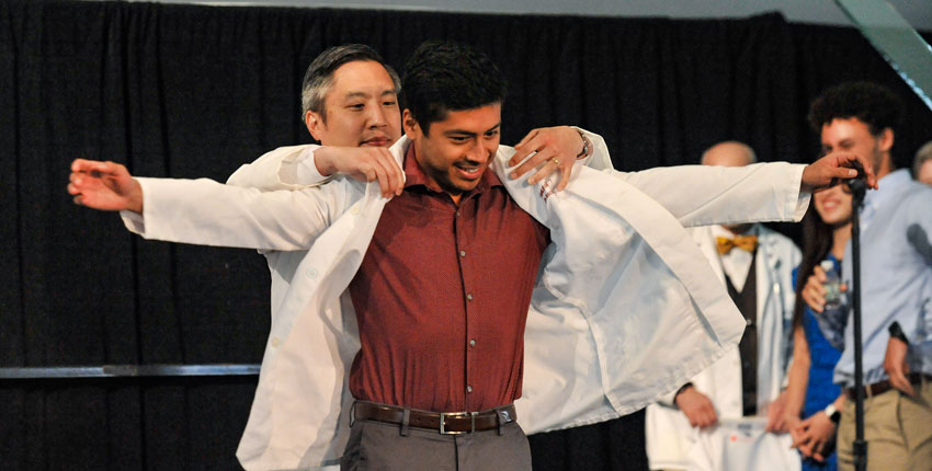 Chang, left, helps a student don his jacket during white coat ceremonies in 2021.  Image: Steve Lipofsky