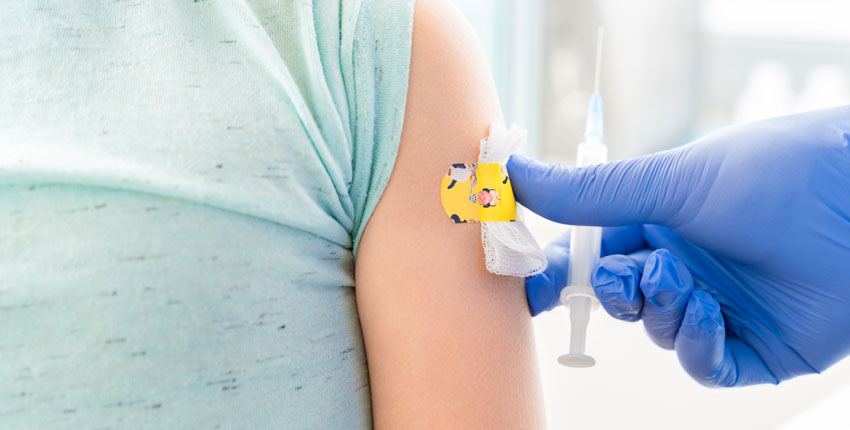Photo of a child's torso with a bandaid on the arm and a blue glove with syringe