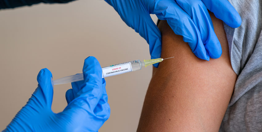 Image of gloved hands administering a vaccine shot to an arm 