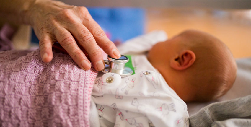 Photo of a hand with a stethoscope on a newborn baby's chest 