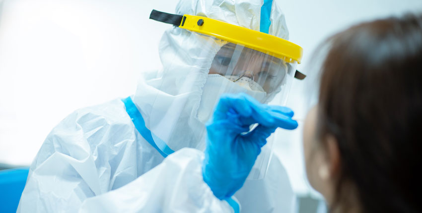 Person in full PPE obtaining a nasal swab specimen from a patient