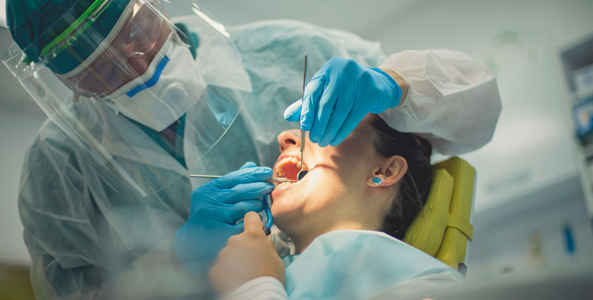 Dentist in full PPE with his hands inside a female patient's open mouth