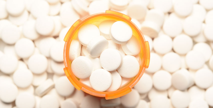 An aerial shot of an orange pill bottle filled with white round pills, surrounded by more of the same pills