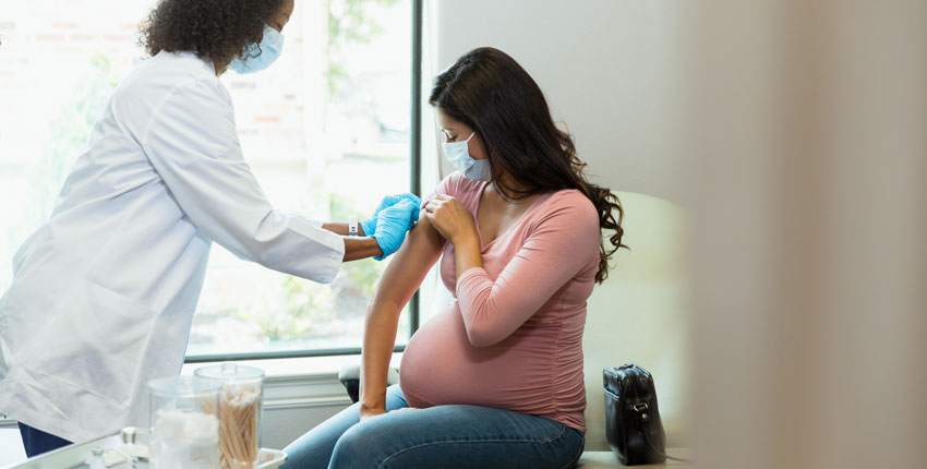 A doctor prepares a pregnant person's arm for a vaccine