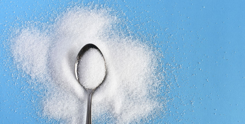 Photo of a spoon of sugar against a blue background