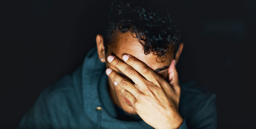 A close up of a person with their hand covering their face against a black background