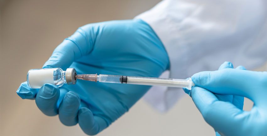 Blue-gloved hands holding a vaccine syringe