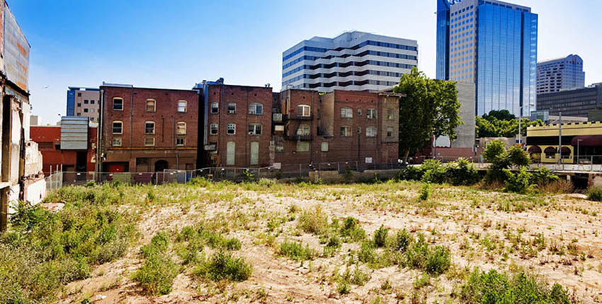 Urban setting showing older low-rise brick housing wedged between an empty dirt lot and modern glass-sided high-rise buildings
