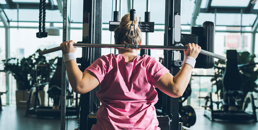Photo of woman in pink top lifting weights in a gym