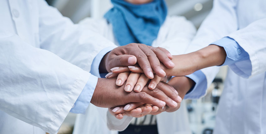 Close up of the stacked hands of three physicians with different ethnicities in solidarity.