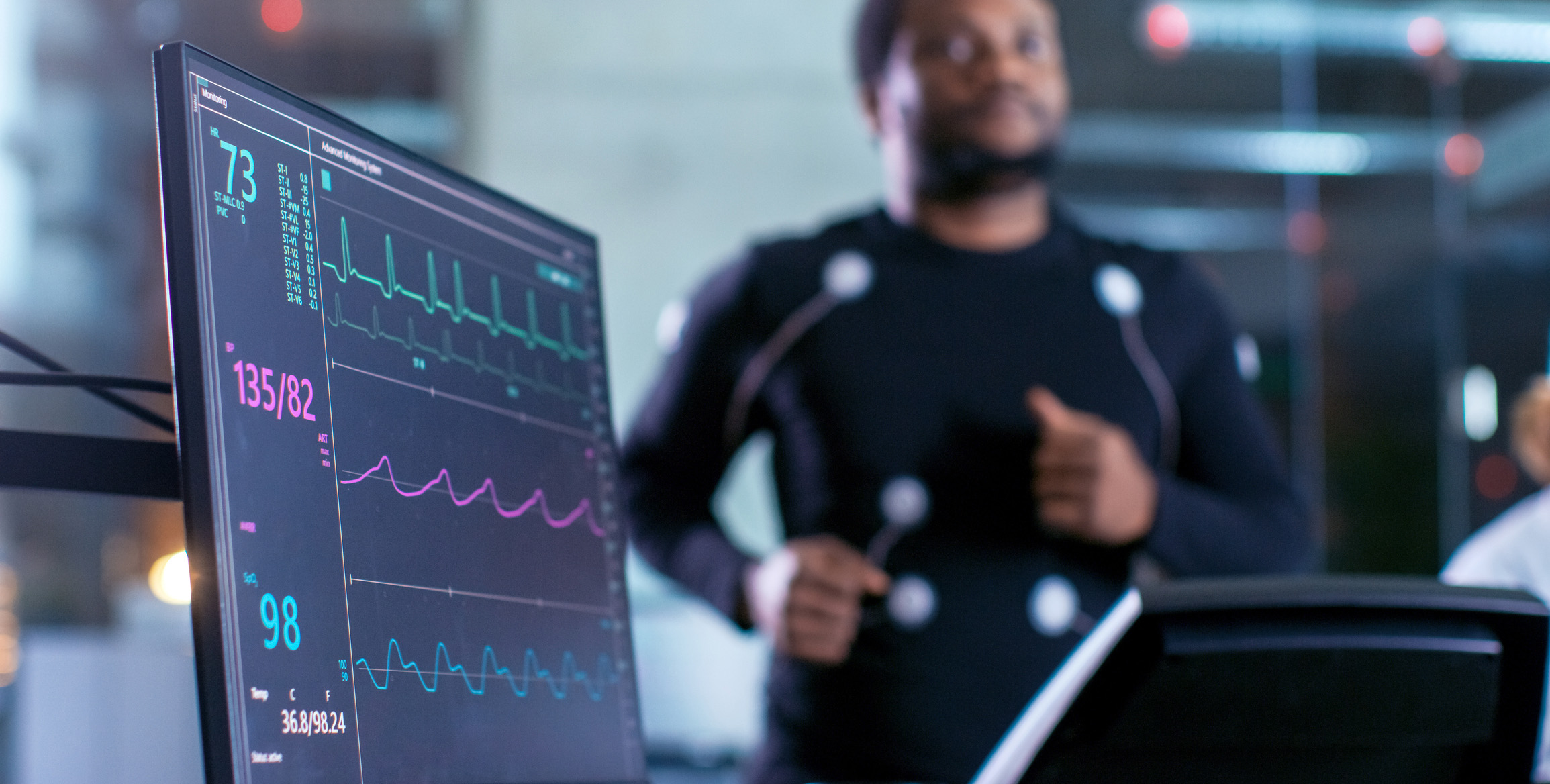 Blurred image of a man on a treadmill with electrodes attached and connected to a heart monitor in a research lab