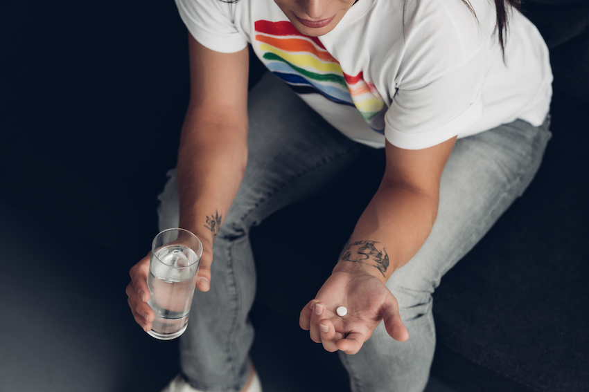 young transgender man with pill and glass of water sitting on couch 