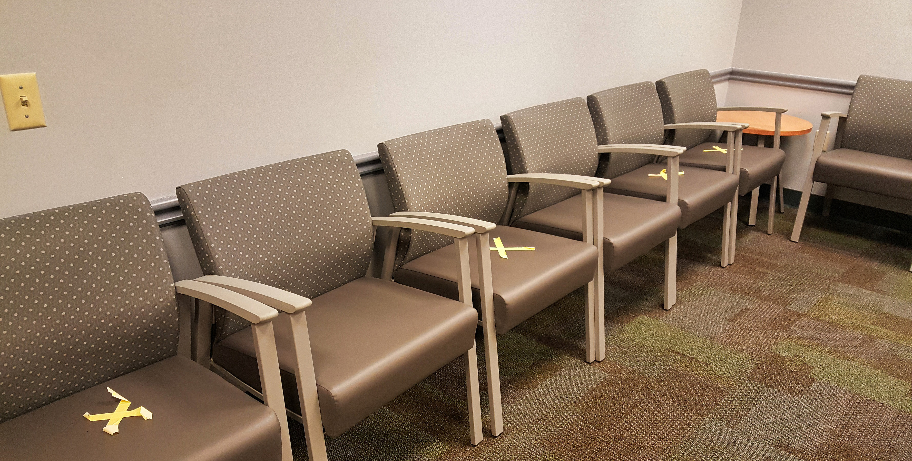 Empty chairs in waiting room, marked with X's for social distancing