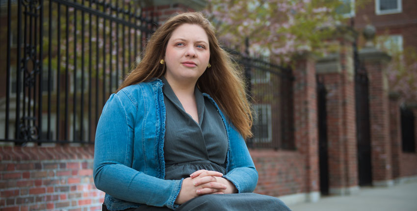 Cloutier sitting in wheel chair with arms folded in lap wearing a green button down and aqua sweater