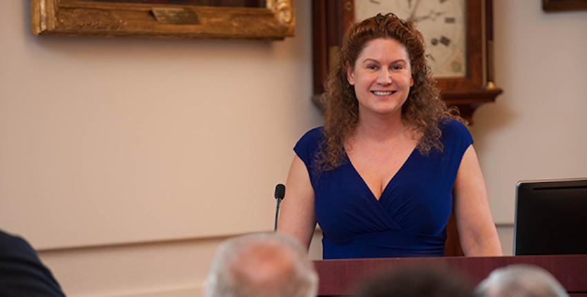 Woman in a dress stands at a podium in front of audience members