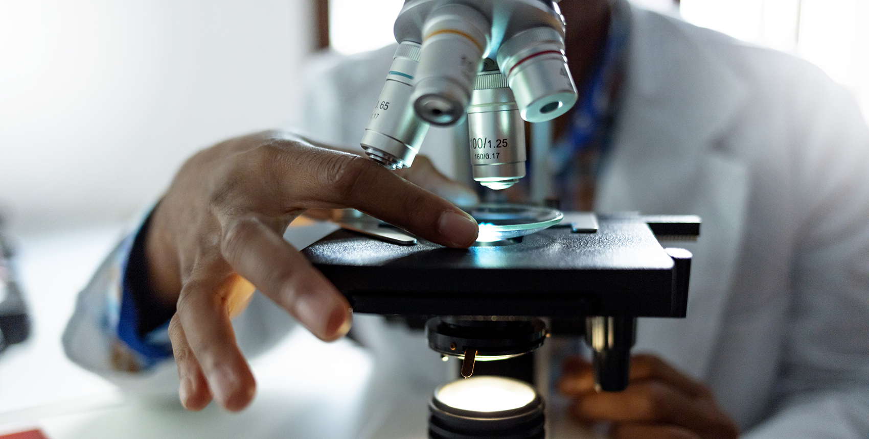 Closeup on the hands of a man in a white lab coat looking in microscope in a medical laboratory.