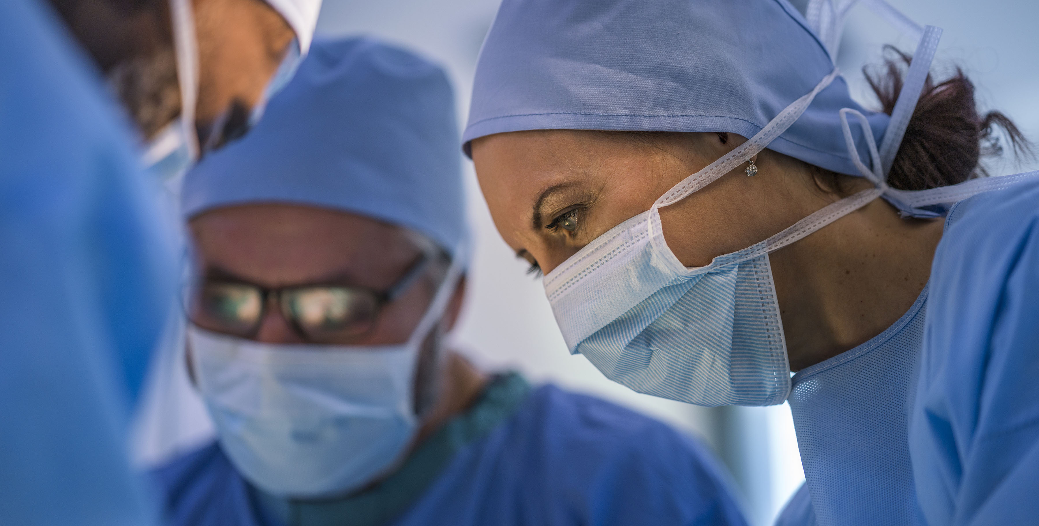 A woman in a surgical mask in the foreground, with men out of focus in the background.