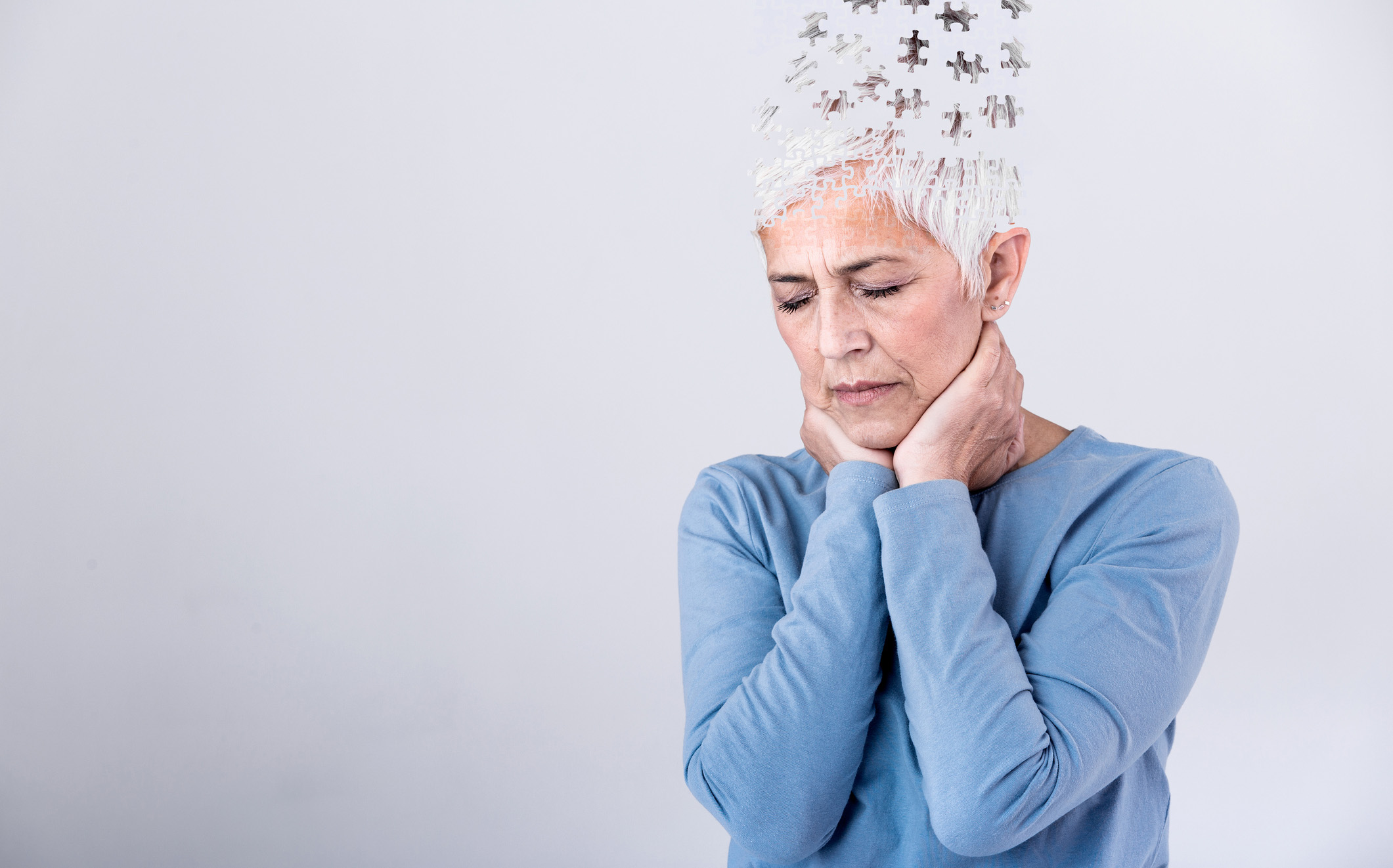 Photo of a distressed woman with short gray hair with illustration puzzle pieces flying out of the top of her head