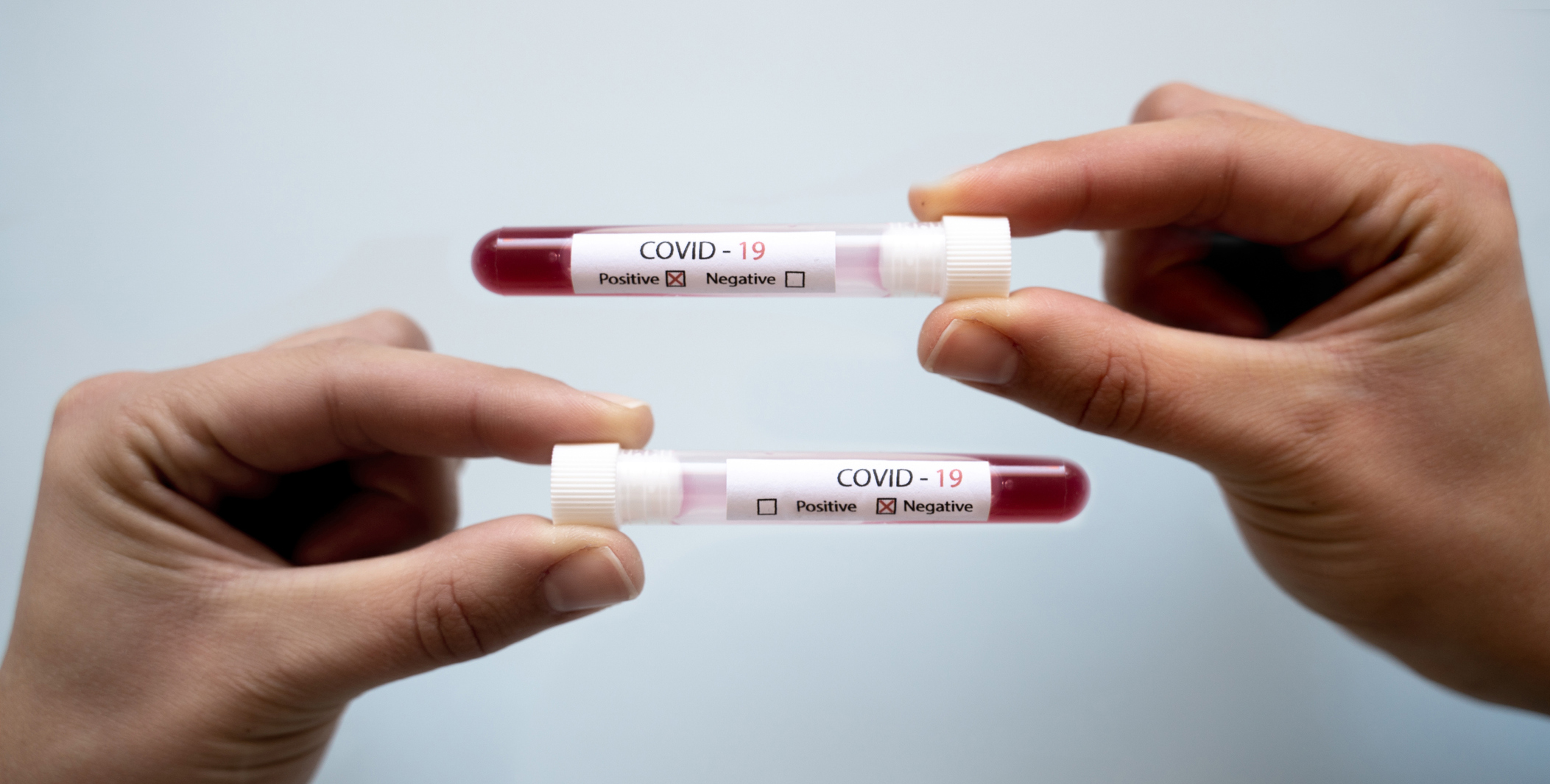 Two hands, each holding a covid-19 blood test, one negative, one positive