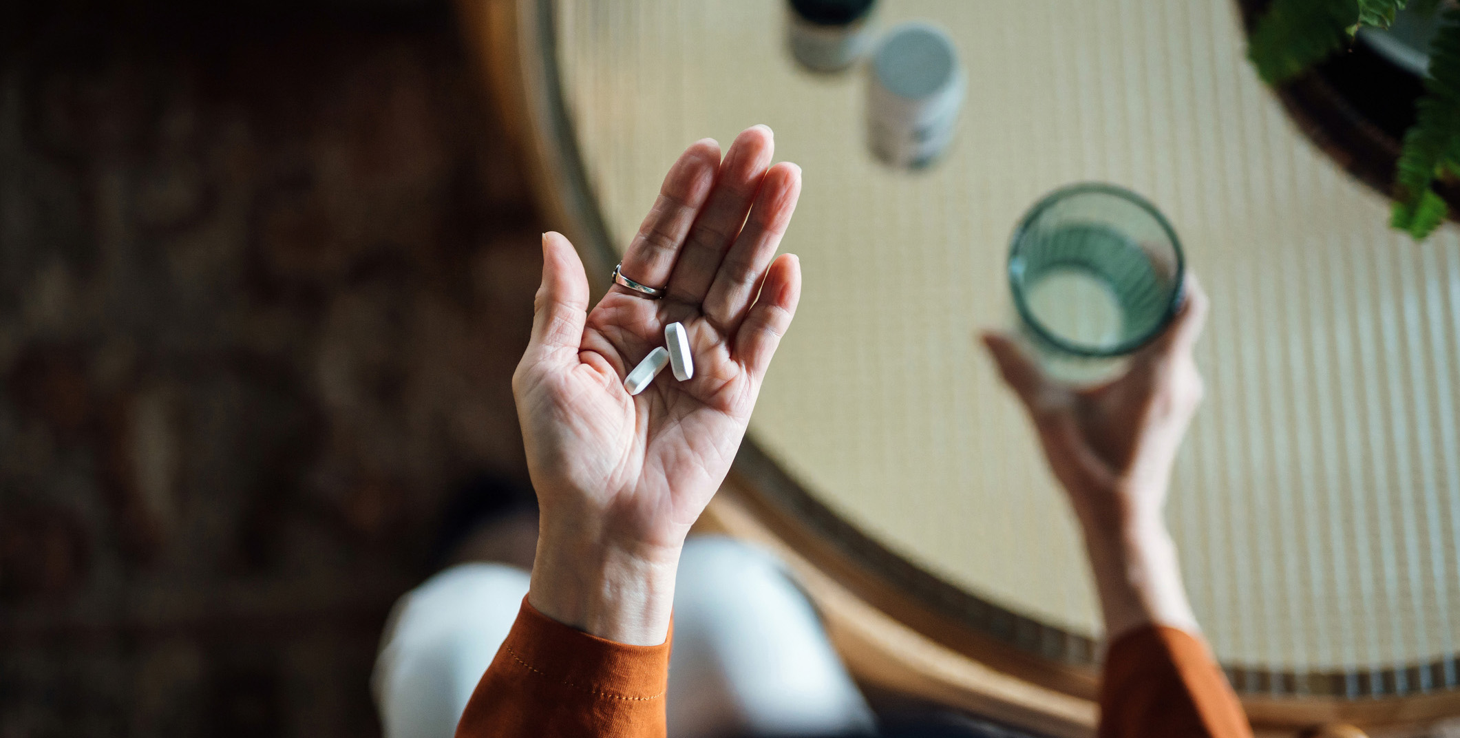 Photo looking down to a woman's hands, one holding a glass of water, in the other hand, some pills