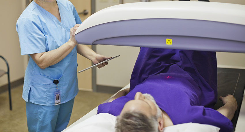 Photo of a gray-haired man lying on an exam table while a technician adjusts a scanning machine over him