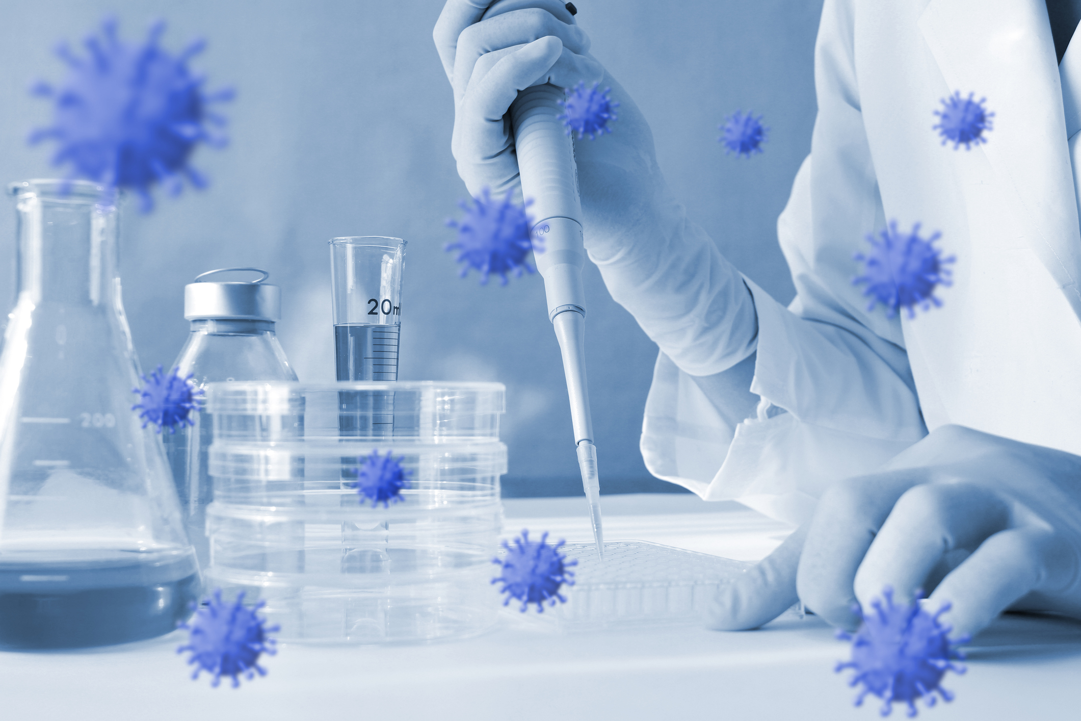 Photoillustration of coronavirus floating around lab equipment with person holding a pipette