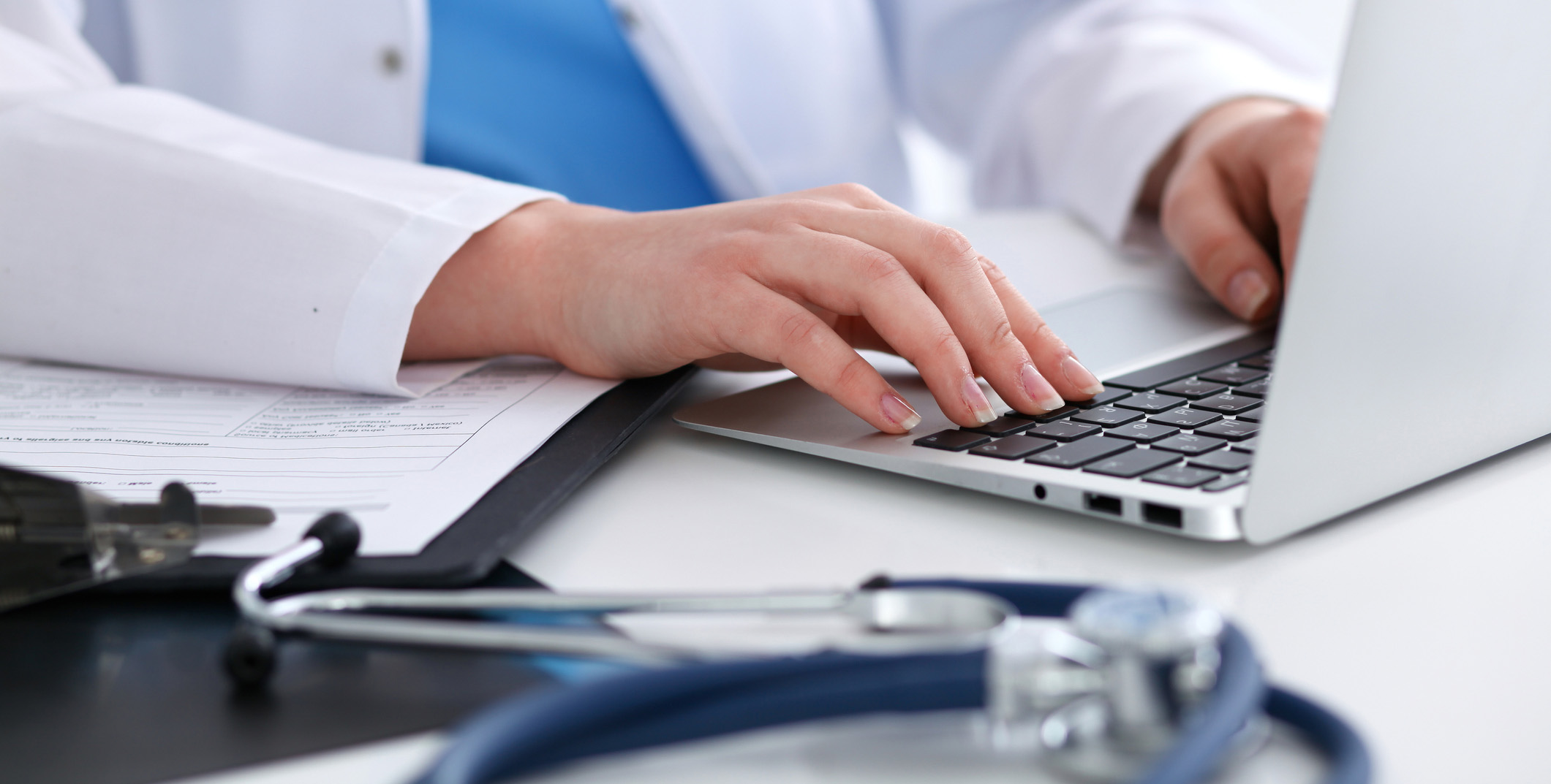 Photo of a physician's hands typing on a keyboard; stethoscope on desk