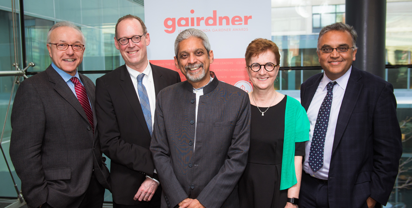Four men and a woman smiling in front of a backdrop for the Gairdner Foundation.