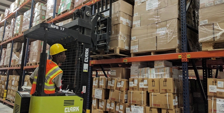 A man operates a forklift loaded with boxes in a warehouse.