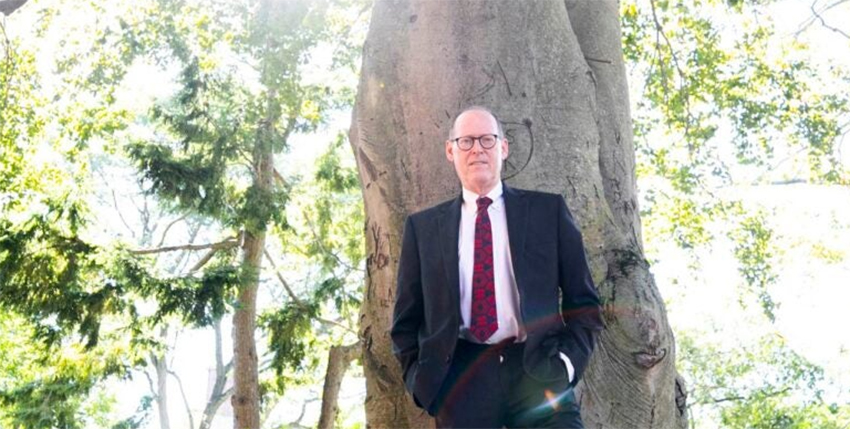 Paul Farmer stands against the front of a tall tree.