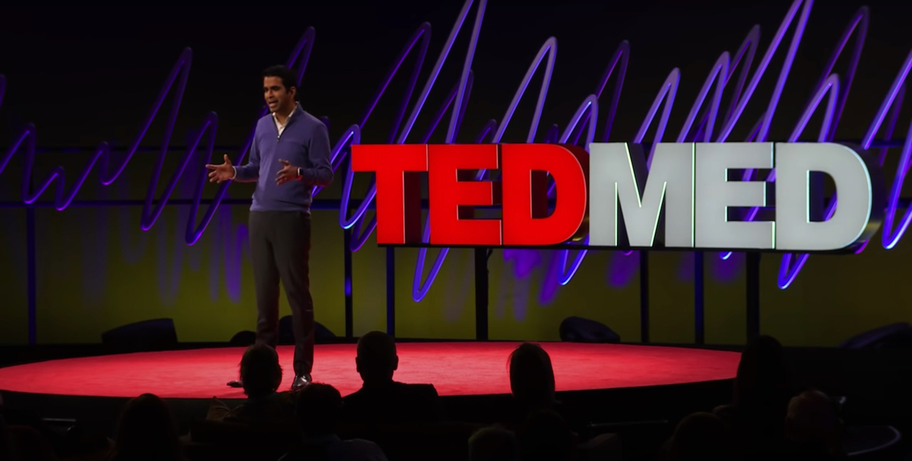 A man speaks on a stage in front of a sign that says TEDMED.