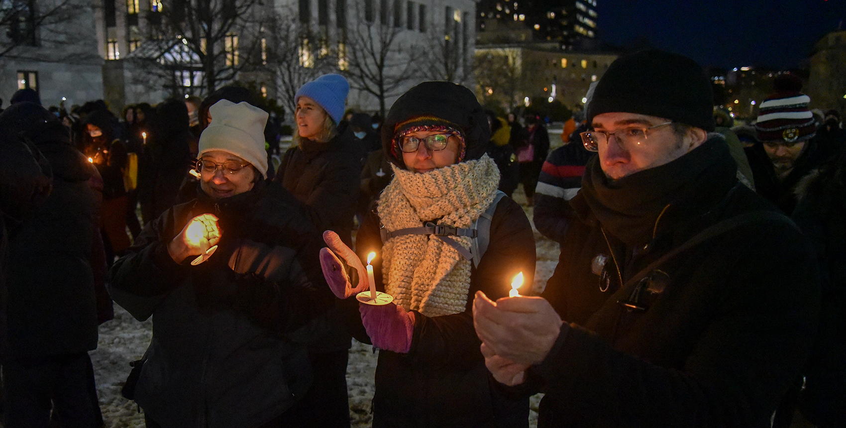People outdoors on a snowy night wearing warm clothes and holding glowing candles
