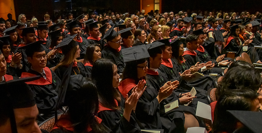 Audience shot of graduates in black and red regalia