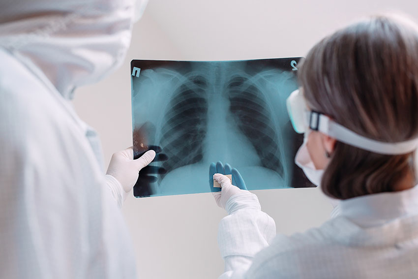 two clinicians in white coats and masks examine X-ray image