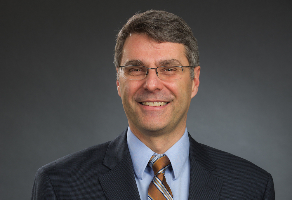 Mark Namchuk in suit and tie against a gray backdrop