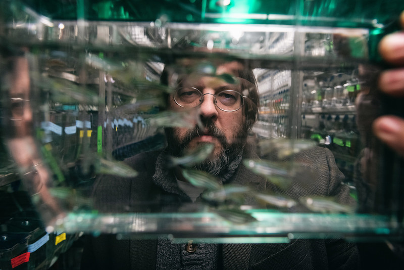 Portrait of a bearded man in glasses through a fish tank he is holding