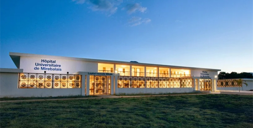 A white hospital building with golden glowing windows under a dark sky.