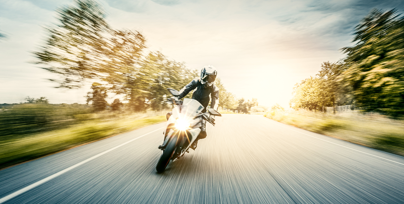 Motion blurred photo of a backlit motorcycle on a tree-lined road.