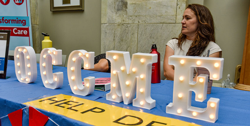 A women sits behind a table with lit up signage letters the spell out OCCME