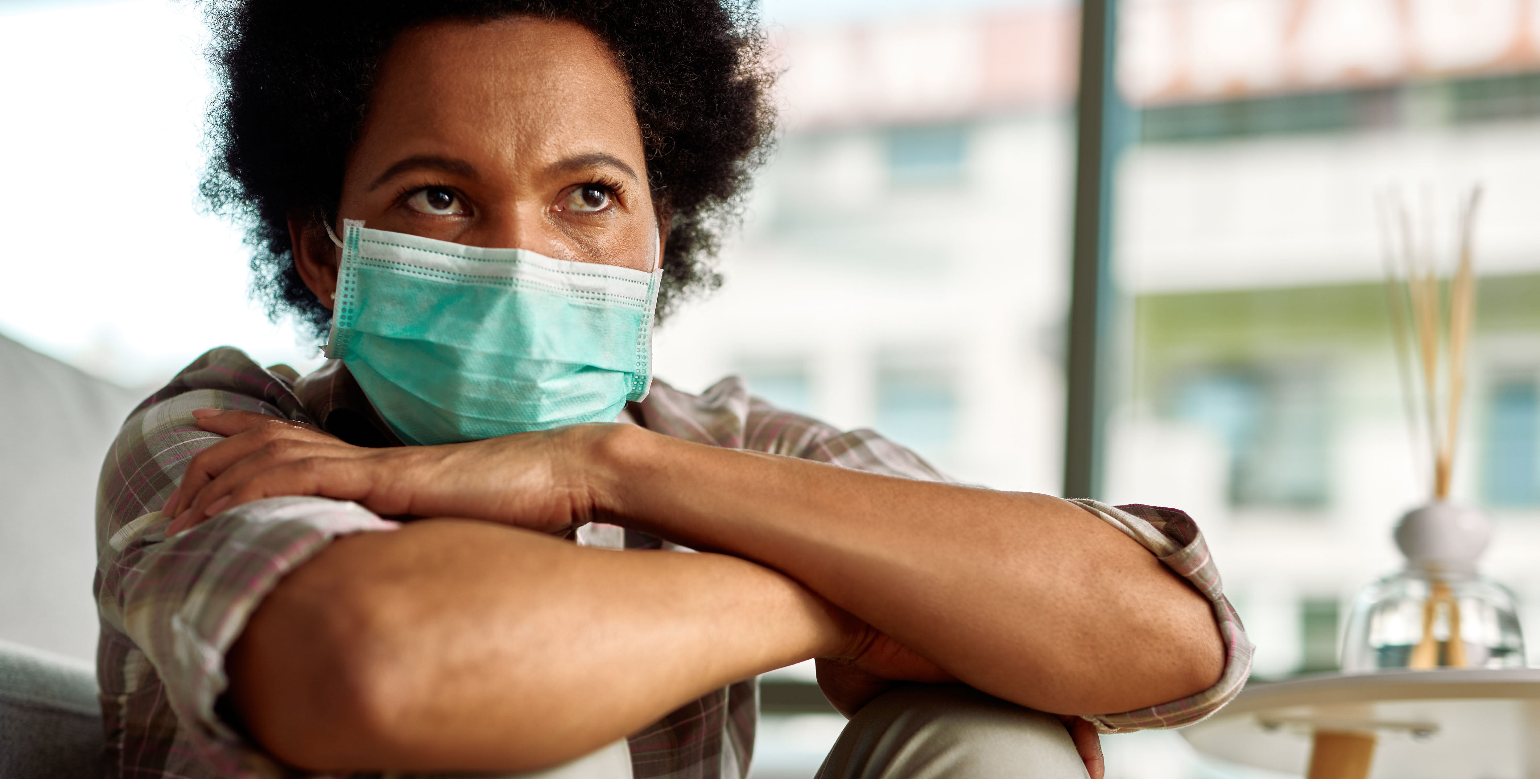 A woman wearing a surgical masks sits with her arms crossed