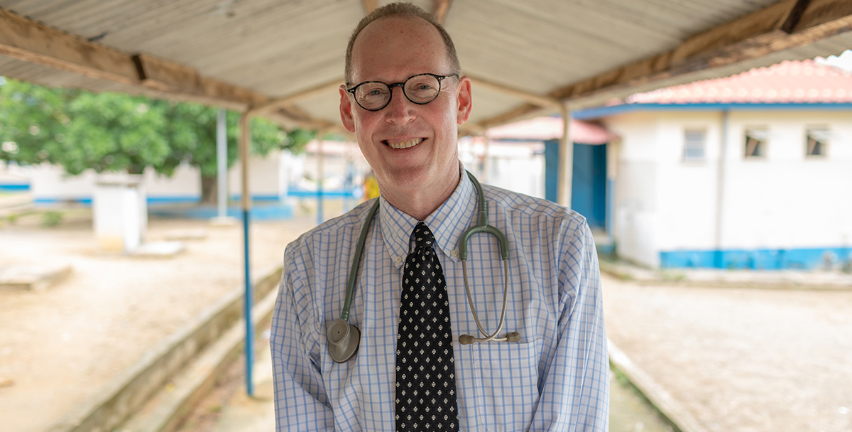 A man sits under a roof with a stethoscope draped around his shoulders.